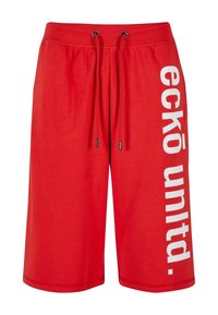 Red athletic shorts with an elastic waistband and adjustable drawstrings. Features a bold white graphic text on the left side. Smooth texture.