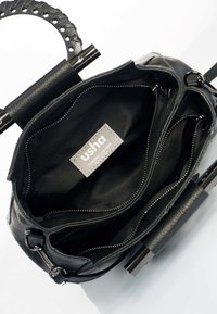 Sac à main en cuir noir avec poignée tressée, compartiments zippés ouverts et étiquette "usha cuir véritable" à l'intérieur.