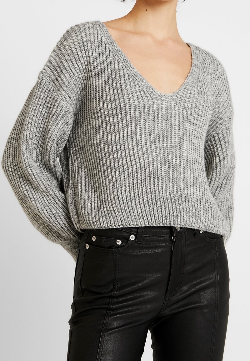 Ljusgrå stickad tröja med V-ringning och lös passform. Matcher med svarta tajta byxor i konstläder med tryckknappsdetaijler.