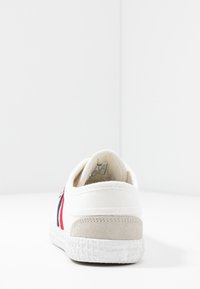 White canvas sneaker with red and navy stripes, textured grey suede heel, and white rubber sole featuring a woven pattern.