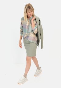 Lightweight plaid shirt in pastel colors, paired with a green pencil skirt. Model wears beige sneakers and holds a matching jacket.