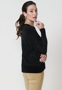 Črn pulover z teksturo in rebrastim robom ter manšeti. Dolgi rokavi in okrogla ovratnica. Uporabljen z bež kordnim hlačami.