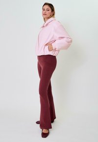 Giacca cropped rosa chiaro con colletto alto e zip, abbinata a pantaloni svasati bordeaux. Styling con scarpe con tacco a blocco rosso scuro.