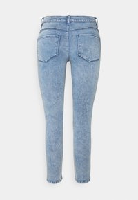 Vaaleansiniset, korkea vyötärö skinny-farkut takataskuilla ja vyölenkeillä, nähtynä takaa valkoista taustaa vasten.