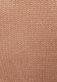 Strickstoff in sanftem Beige, mit einem strukturierten Muster aus gleichmäßigen, regelmäßigen Stichen, das ein leicht dehnbares und gemütliches Erscheinungsbild erzeugt.