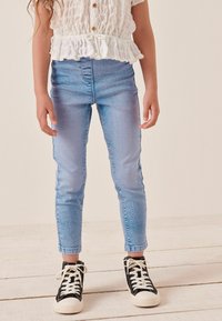 Ljust blå denim slim jeans med hög midja och subtila blekningar, matchade med svarta höghögar sneakers med vita snören.