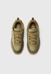 Et par olivengrønne Puma sneakers med brune såler, snørebåndsdesign og polstrede kraver placeret side om side på en hvid baggrund.