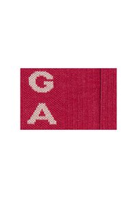 Tessuto rosso con lettere ricamate bianche "G", "A" e "A". La texture appare liscia, con una leggera lucentezza del materiale.
