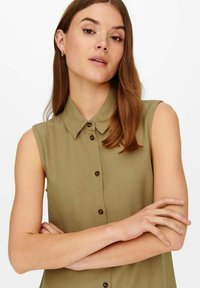Mouwloze, olijfgroene blouse met een knoopsluiting aan de voorkant, een klassieke kraag en een gladde textuur, met donkere knopen en een getailleerde pasvorm.