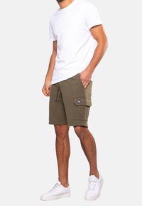 Olijfgroene cargoshorts met een gestructureerde afwerking, elastische tailleband en voorzak. Gecombineerd met een eenvoudige witte T-shirt en witte sneakers.