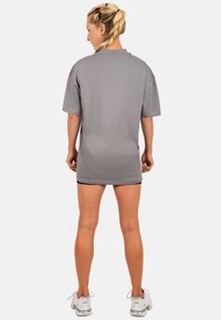Grijze oversized t-shirt met korte mouwen en een afgeronde zoom. De stof lijkt zacht met een minimale textuur. Model draagt zwarte shorts en sneakers.