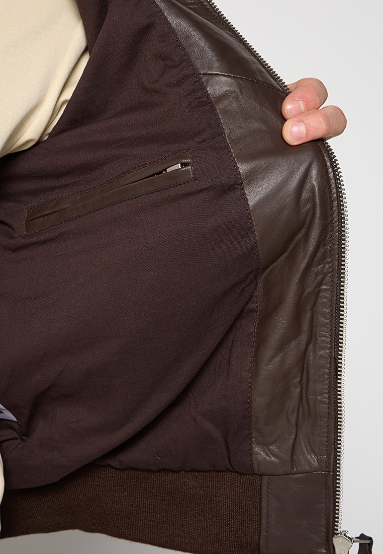 Intérieur d'une veste en cuir et tissu marron avec une texture brun foncé, poche zippée, couture visible et détail de bord côtelé.