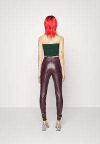 Pantaloni in finta pelle bordeaux con vestibilità slim, abbinati a un top corto verde scuro. La modella indossa tacchi quadretti bianco e nero.
