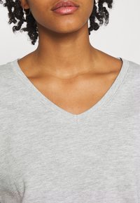 T-shirt grigia con scollo a V realizzata in tessuto morbido, caratterizzata da un design minimalista e una texture sottile, con un colletto rilassato.