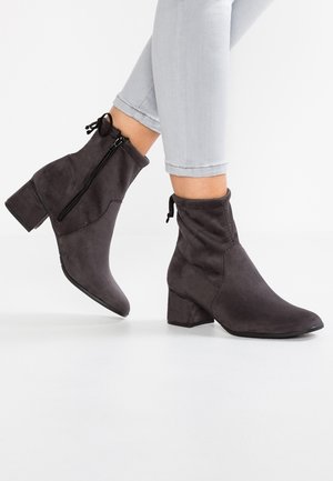 Szare zamszowe botki za kostkę na słupku, z bocznym zamkiem błyskawicznym i elastycznym wykończeniem u góry. Charakteryzują się gładką fakturą i szpiczastym noskiem.