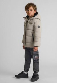Ljusgrått pufferjacka med huva, med dragkedja framtill och elastiskaHandledningar. Bärs över mörkgrå cargobyxor med sidofickor och svarta sneakers.