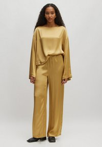 Goldfarbener Satin-Loungewear-Set mit einem locker sitzenden Oberteil mit weiten Ärmeln und einer Hose mit elastischem Bund. Glatte Textur und minimalistisches Design.