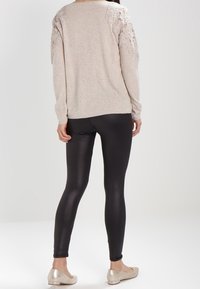 Beige Pullover mit floralen Spitzenakzenten an den Ärmeln, schwarze Leggings und flache metallische Schuhe. Glatte Texturen und taillierte Passform.
