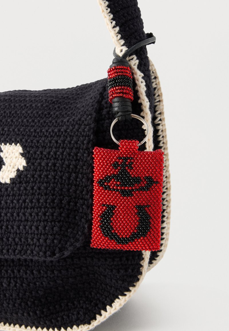 Black crocheted bag with cream stitching and a red beaded keychain featuring black symbols hanging from the strap.