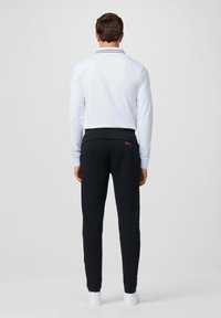 Witte lange mouwen polo met een kraag en marineblauwe strepen; zwarte joggingbroek met elastische tailleband en rood logo; witte sneakers.