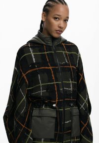 Karomuster oversized Kapuzenjacke in Dunkelgrün, Schwarz und Orange mit gesteppten Details, zwei Fronttaschen und einem verstellbaren Kordelzug in der Taille.