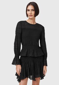 Schwarzes Kleid mit langen gerüschten Ärmeln, geschichtetem Peplum-Taille und ruffled Saum. Hergestellt aus leichtem, strukturiertem Stoff.