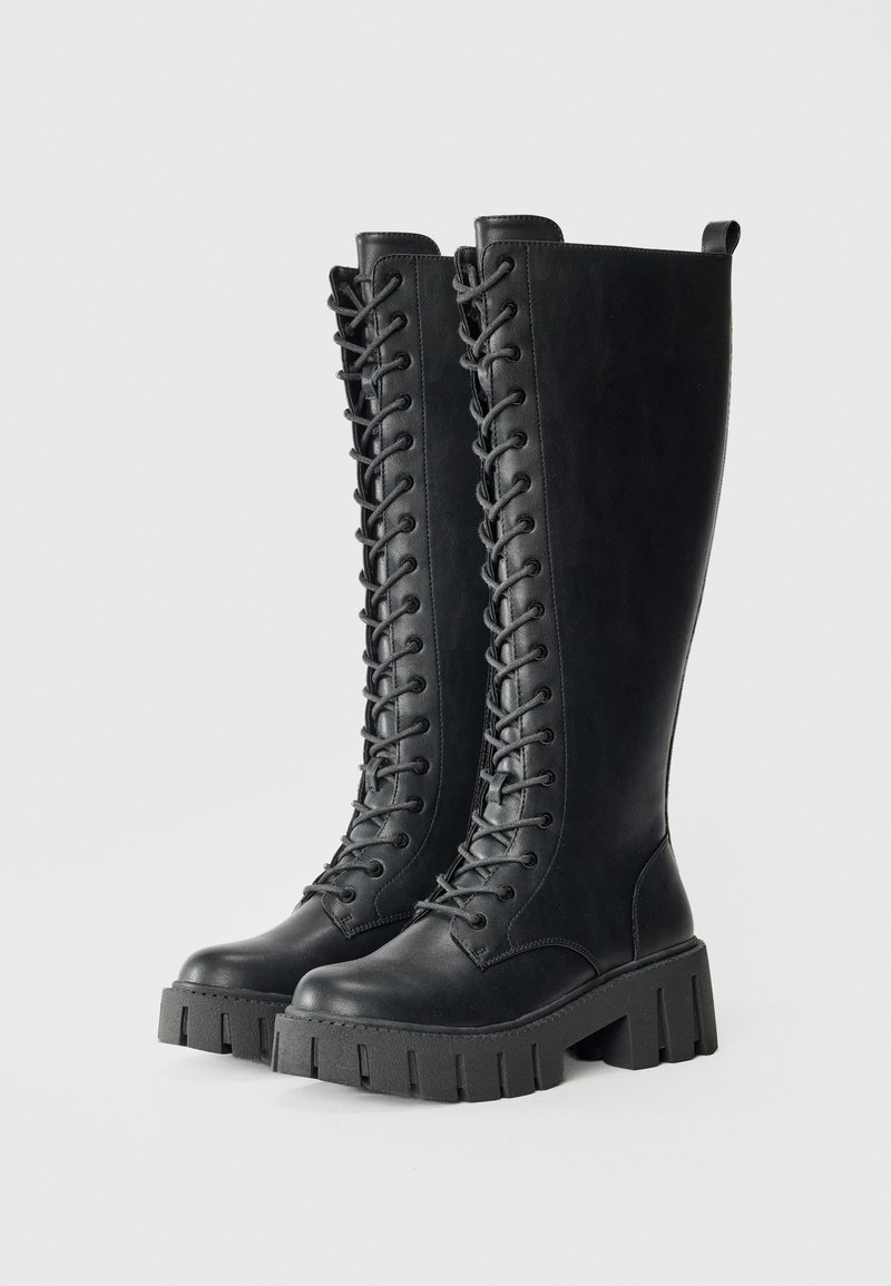 Bottes noir en cuir hautes jusqu'au genou avec lacets à l'avant, semelle à plateforme texturée et une languette en haut pour un enfilage facile.