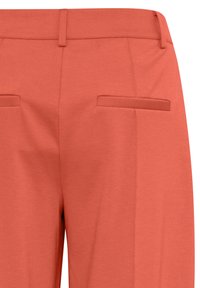 Pantalons de couleur pêche avec une texture lisse, dotés de deux poches arrière et d'un design à coupe droite. Coutures visibles le long de la taille.