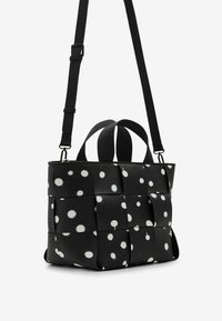 Sac tissé noir avec un motif de pois blancs, deux anses supérieures et une bandoulière réglable. Fabriqué en matériau texturé.