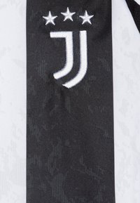 Tessuto a righe bianche e nere con un prominente logo ricamato della Juventus e tre stelle sopra, che indicano i successi.