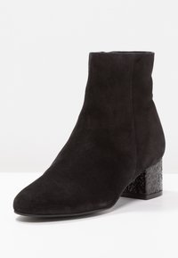 Schwarze Wildleder-Ankle Boots mit spitzer Zehe und strukturiertem Blockabsatz. Glatte Oberfläche im oberen Bereich, mit kontrastierenden glänzenden Absatzakzenten.