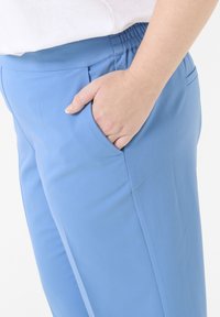 Light blue, elastic-waist pants with a side pocket, smooth texture, tailored fit, and minimal stitching details.