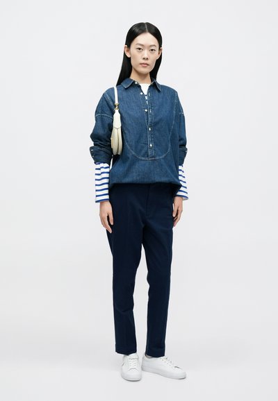 Πουκάμισο τζιν με πλατύτερη εφαρμογή, μανσέτες με ρίγες σε μπλε και άσπρο, συνδυασμένο με ναυτικό μπλε παντελόνι και λευκά αθλητικά παπούτσια. Απλή τσάντα ώμου.