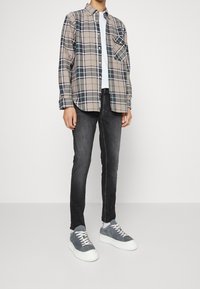 Camisa de franela a cuadros en beige, azul marino y verde; jeans ajustados gris; zapatillas de ante gris con suelas y cordones blancos; atuendo informal.