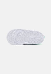 Sohle eines weißen Sneakers mit runden und rechteckigen Profilmustern, die in der Mitte ein kleines erhabenes Jumpman-Logo aufweist.