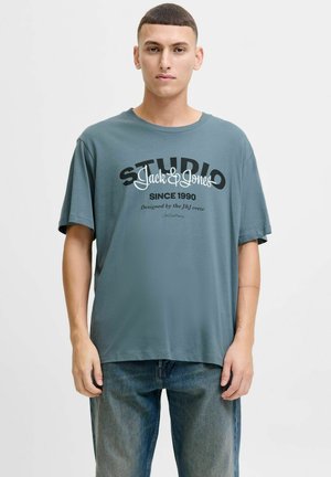 Grå bomulds t-shirt med korte ærmer, der har sorte og hvide grafikker, der står "STUDIO Jack & Jones" og "SINCE 1990."