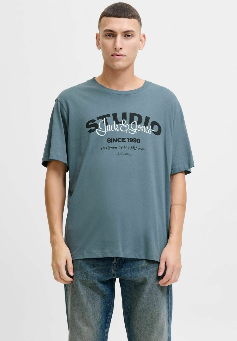 Grå bomulds t-shirt med korte ærmer, der har sorte og hvide grafikker, der står "STUDIO Jack & Jones" og "SINCE 1990."