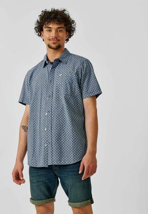 Kortærmet skjorte i marineblå med et hvidt prikkemønster, med knaplukning foran og en enkelt brystlomme. Blødt stof, afslappet pasform.