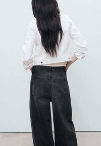 White cropped denim jacket with rolled sleeves paired with high-waisted black wide-leg jeans featuring back pockets. Smooth fabric texture.