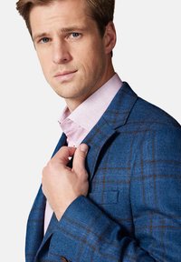 Niebieski marynarka w kratę, wykonana z teksturowanej tkaniny, z brązowymi akcentami. Nosi się ją na jasnoróżowej koszuli w wzory, z klapami.