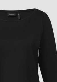 Schwarzes Langarmoberteil aus weichem Stoff, mit weitem Ausschnitt und einfachem Design, minimalen Details und einem Etikett innen.