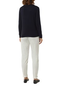 Marineblauwe pullover trui met lange mouwen, ribbels aan de manchetten en onderrand, gecombineerd met witte broeken en zwarte platte schoenen in een casual setting.