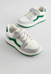 Hvide sneakers med grå og grønne detaljer, der har en glat overflade, afrundet form, gummisål og justerbar rem.