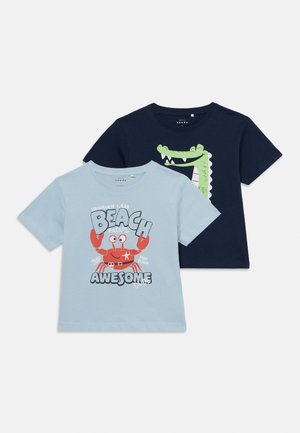 Due magliette a maniche corte: una azzurra chiaro con una grafica di granchio e testo, l'altra blu navy con una grafica di coccodrillo. Tessuto in cotone, design a girocollo.