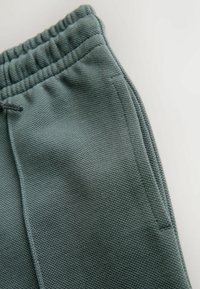 Textured green jogger pants featuring an elastic waistband and drawstring, with side pockets and a straight leg design.