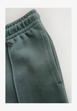 Texturált zöld sportnadrág, rugalmas derékkal és zsinórral, oldalsó zsebekkel és egyenes lábtervezéssel.