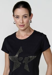 Zwarte katoenen t-shirt met een ronde halslijn, voorzien van een sterontwerp gemaakt van zilveren rhinestones aan de voorkant. Korte mouwen, slim fit.