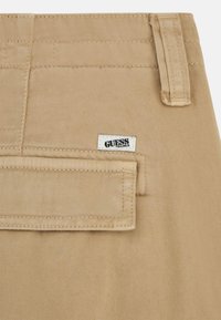 Beige katoenstof met diagonale ribbelstructuur, voorzien van een ruitzak en een klein GUESS-label genaaid op de tailleband.