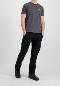 Šedé tričko s kulatým výstřihem a zeleným logem, spárované s černými cargo kalhotami s bočními kapsami. Černé tenisky dotvářejí celý outfit.