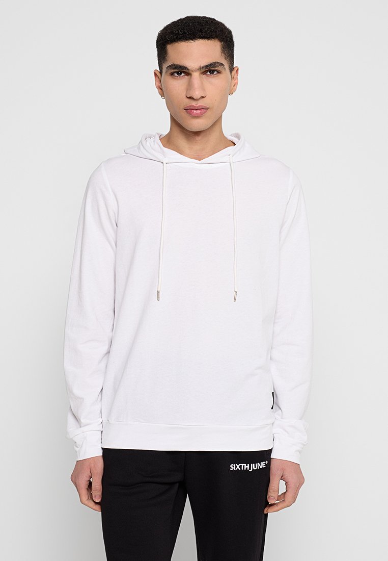 Witte hoodie met een voorzak in kangoeroestijl, met een trekkoord capuchon en lange mouwen; van textuur katoen; gedragen met zwarte joggingsbroek met witte bedrukking.